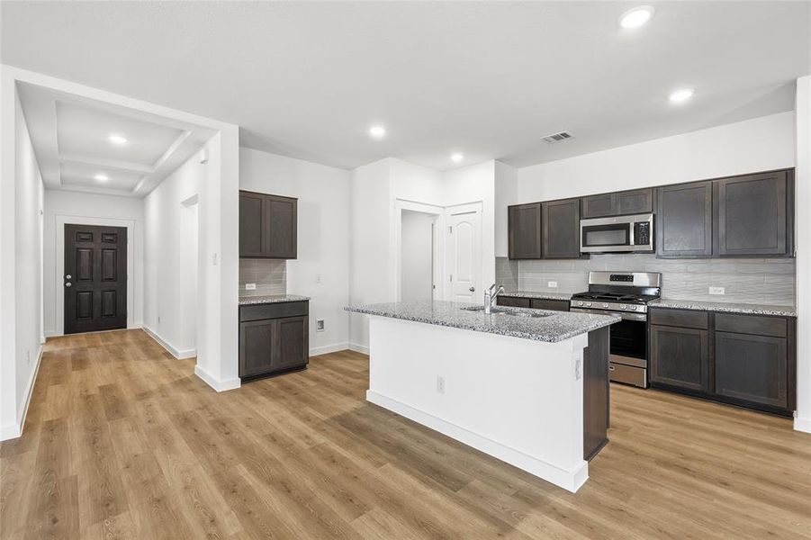 Kitchen with stainless steel appliances, backsplash, light stone countertops, dark wood finish cabinets, and recessed lighting