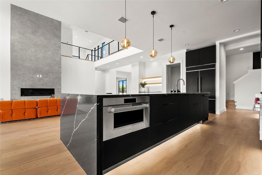 Kitchen with modern cabinets, dark cabinetry, light wood-style flooring, a spacious island, and a high ceiling Kitchen with modern cabinets, dark cabinetry, light wood-style flooring, a spacious island, and a high ceiling
