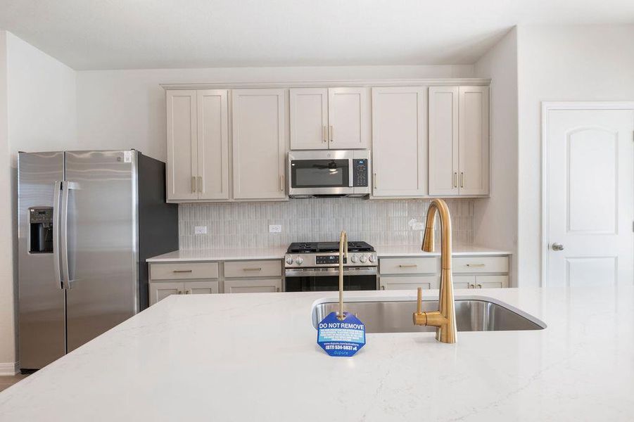 Kitchen with stainless steel appliances, tasteful backsplash, and light stone counters