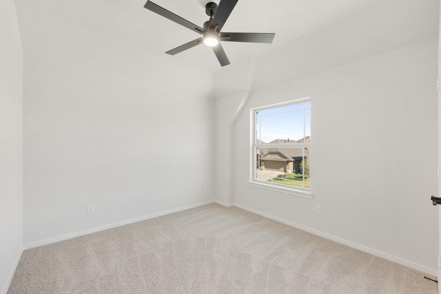 Empty bedroom with vaulted ceiling, ceiling fan, carpet flooring, and a window overlooking neighboring homes. Empty bedroom with vaulted ceiling, ceiling fan, carpet flooring, and a window overlooking neighboring homes.