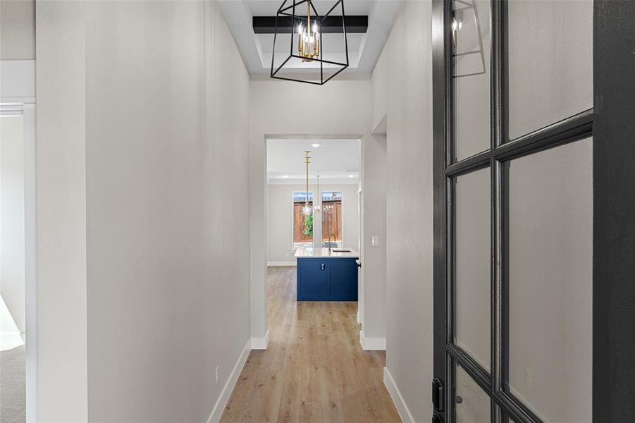 Corridor with light wood-type flooring and a notable chandelier