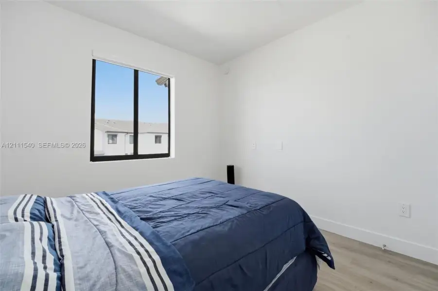 Bright interior room featuring crisp white walls, neutral-toned wood-finish flooring, and a single-pane window with a black frame