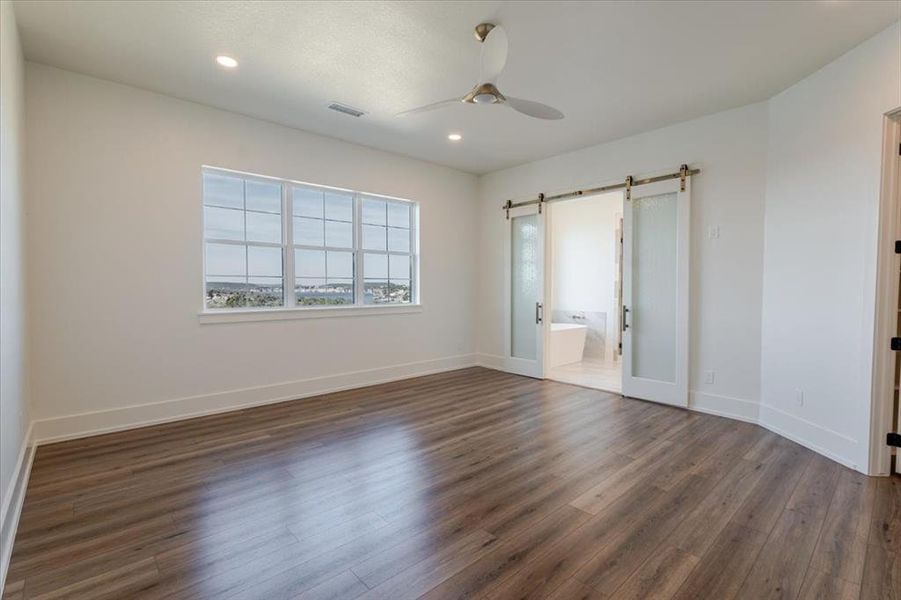 Unfurnished bedroom featuring connected bathroom, dark hardwood / wood-style floors, ceiling fan, and a barn door Unfurnished bedroom featuring connected bathroom, dark hardwood / wood-style floors, ceiling fan, and a barn door
