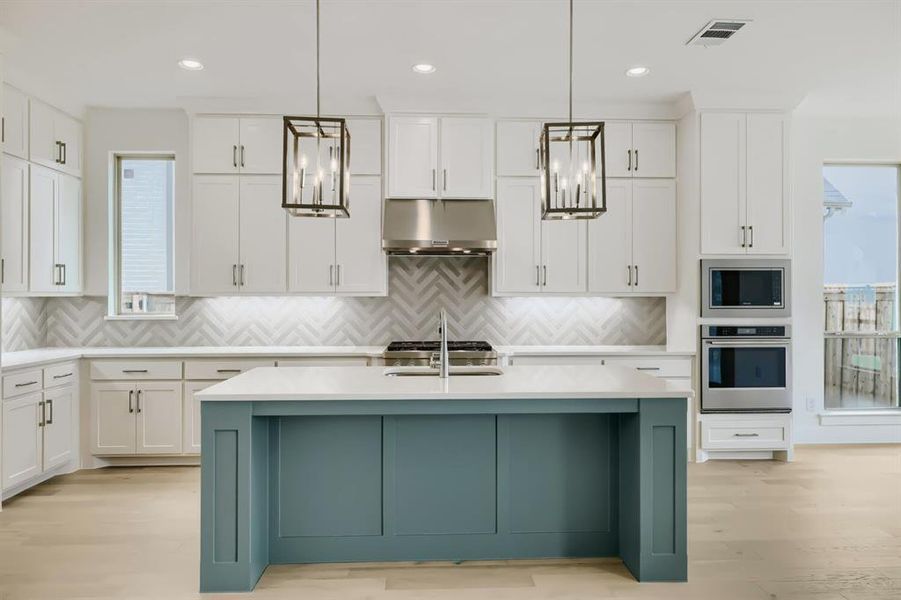 Contemporary kitchen featuring a prominent island with a teal base, white countertops, stainless steel appliances, herringbone tile backsplash, and wood-finish flooring Contemporary kitchen featuring a prominent island with a teal base, white countertops, stainless steel appliances, herringbone tile backsplash, and wood-finish flooring