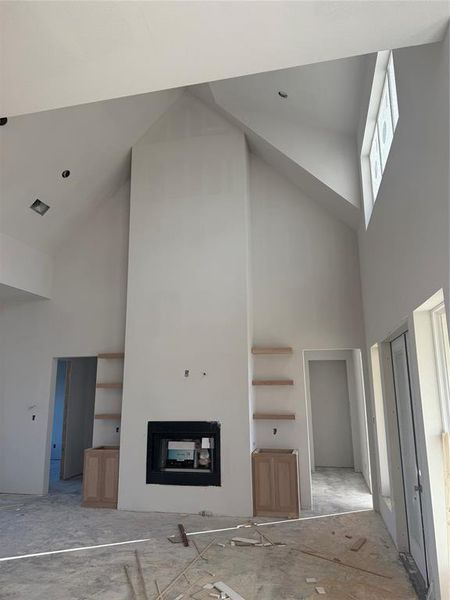 Unfurnished living room with high vaulted ceiling and a glass covered fireplace