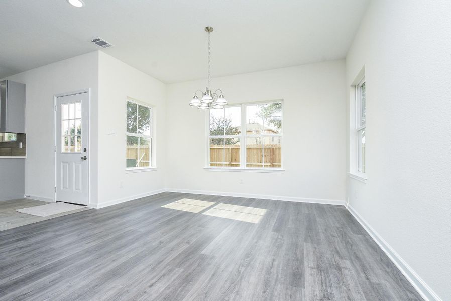 This is a bright, spacious room with modern gray wood flooring, large windows offering plenty of natural light, and a fresh, neutral color scheme. It also features a classic chandelier and a view of a fenced backyard. This is a bright, spacious room with modern gray wood flooring, large windows offering plenty of natural light, and a fresh, neutral color scheme. It also features a classic chandelier and a view of a fenced backyard.