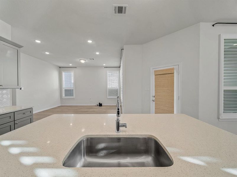 Kitchen featuring light stone countertops, backsplash, gray cabinetry, and sink