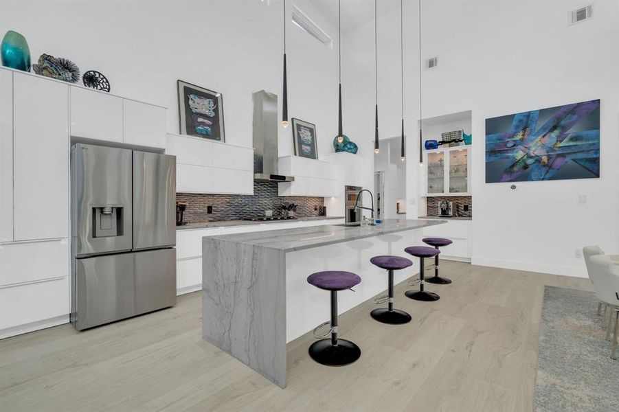 Kitchen featuring a breakfast bar, white cabinets, stainless steel refrigerator with ice dispenser, modern cabinets, and a towering ceiling