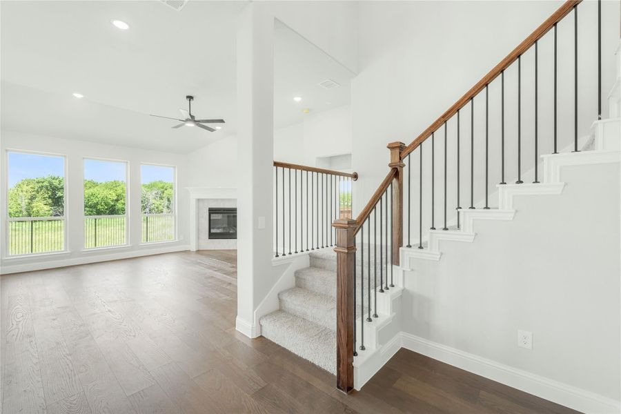 Open living area with wood staircase, iron balusters, hardwood floors, fireplace, and large windows with backyard view Open living area with wood staircase, iron balusters, hardwood floors, fireplace, and large windows with backyard view
