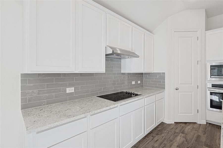 Kitchen featuring light stone counters, dark hardwood / wood-style floors, ventilation hood, white cabinets, and appliances with stainless steel finishes