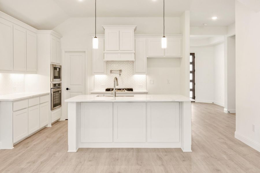 White kitchen with large center island, pendant lights, double wall ovens, and light wood floors