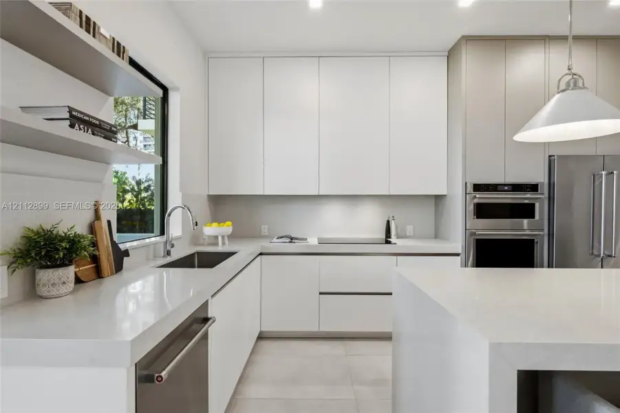 Modern kitchen featuring flat-panel cabinetry, light-toned stone countertops, built-in stainless steel appliances, dual open floating shelves, and an oversized island
