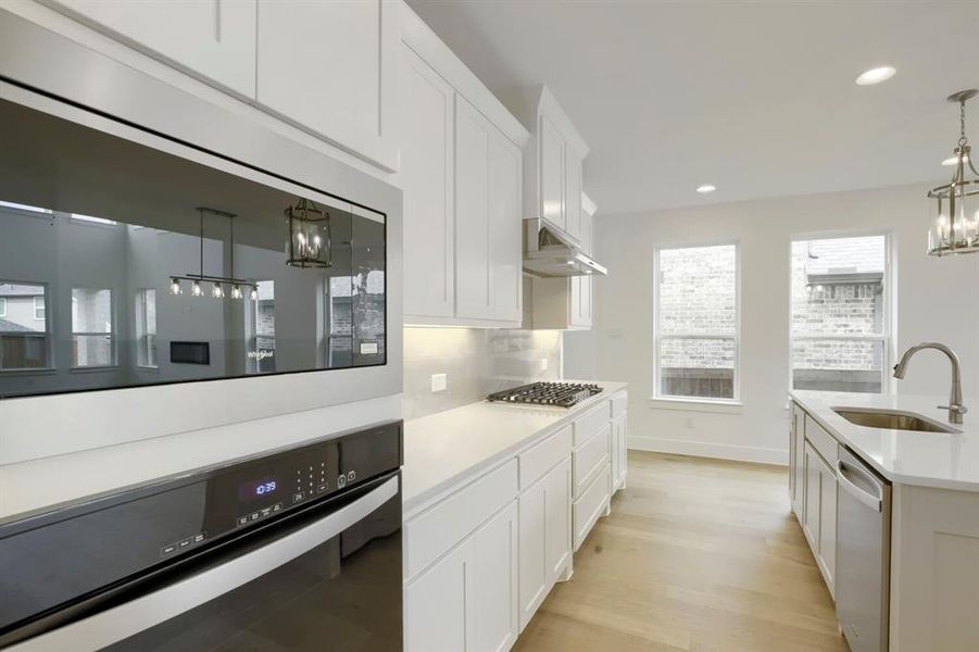 Modern kitchen featuring white cabinetry, light countertops, wood-finish flooring, a stainless steel gas range, and a built-in microwave and oven combination