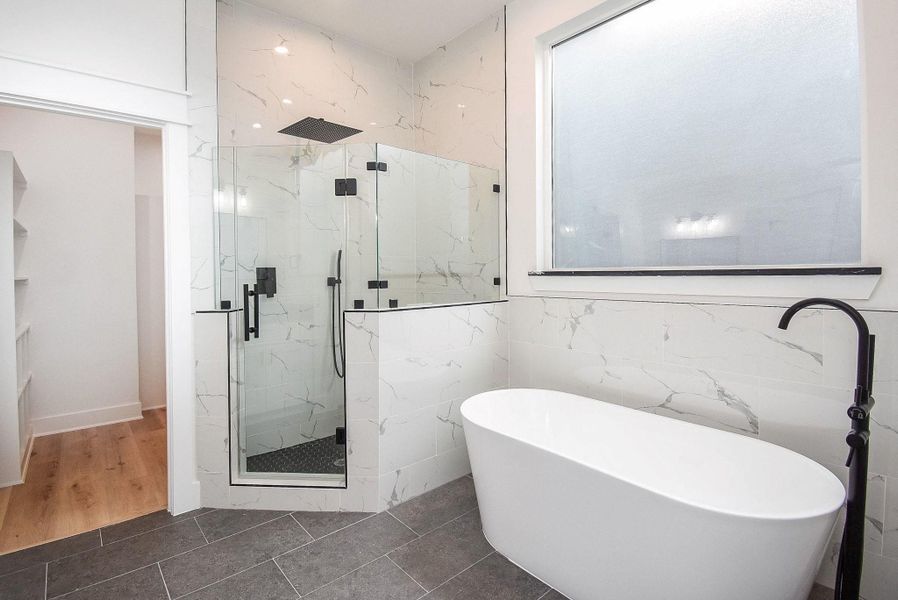 This bathroom features a modern design with a freestanding bathtub, a spacious glass-enclosed shower with marble-style tiles, and large frosted window for privacy. The room is bright and sleek, with a mix of tile and wood flooring.