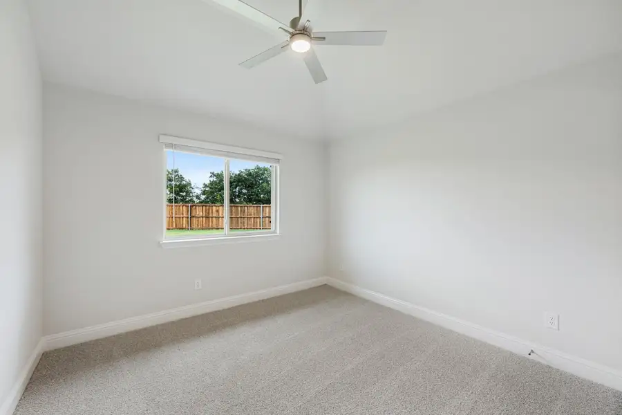 Empty bedroom with carpet flooring, ceiling fan, and a window overlooking a fenced backyard Empty bedroom with carpet flooring, ceiling fan, and a window overlooking a fenced backyard