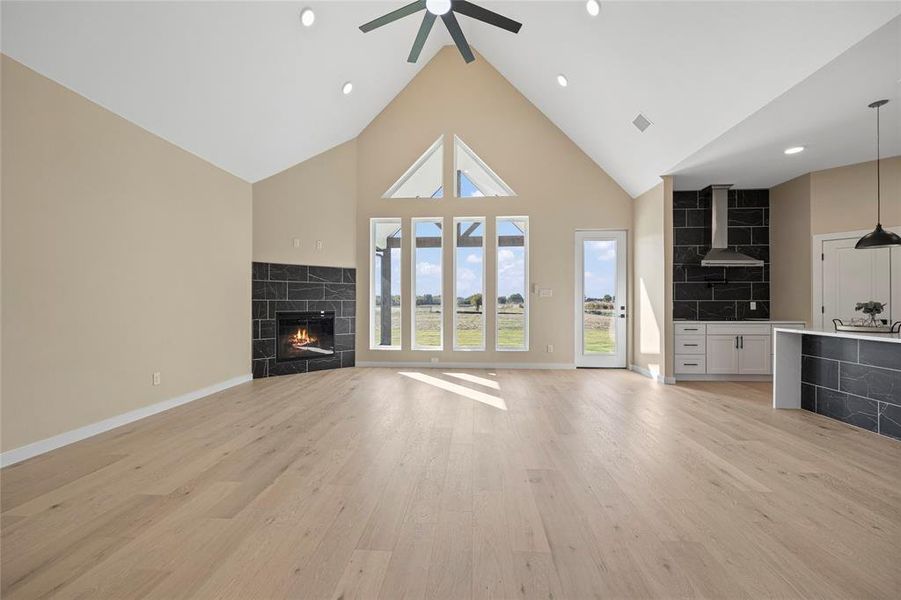 Unfurnished living room with a tiled fireplace, ceiling fan, high vaulted ceiling, and light hardwood / wood-style flooring