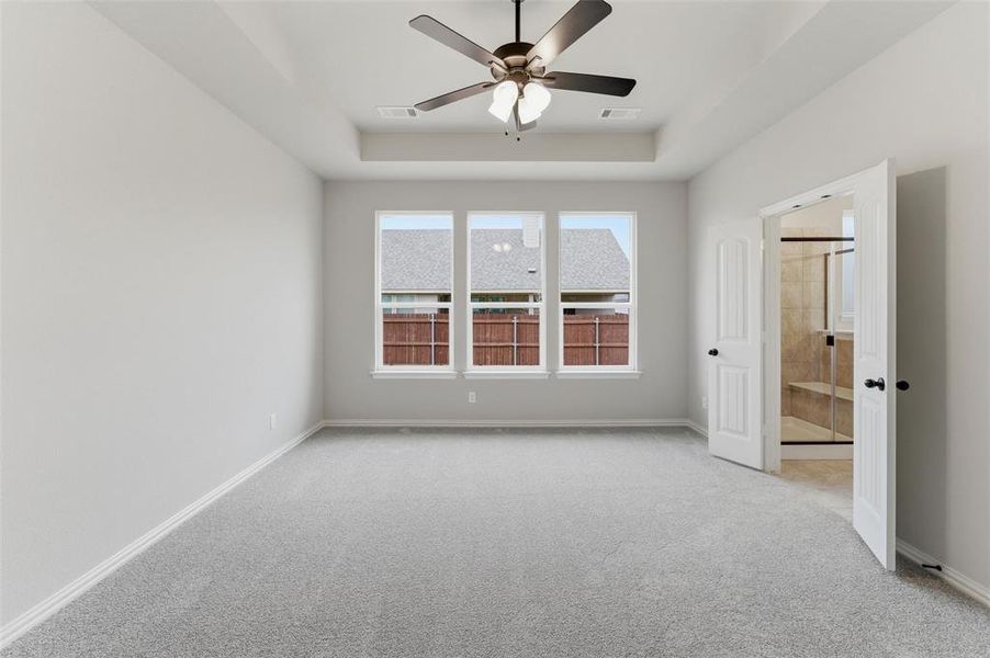 Empty room featuring light colored carpet, a ceiling fan, and a tray ceiling