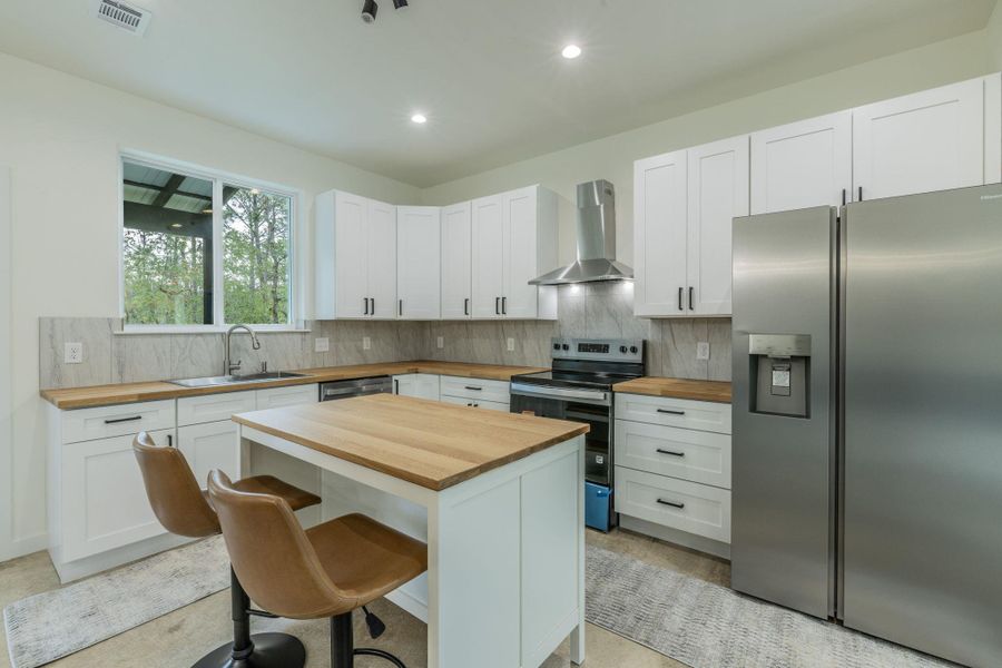 Modern kitchen featuring white cabinetry with dark hardware, natural wood-finish countertops, and a full suite of stainless steel appliances Modern kitchen featuring white cabinetry with dark hardware, natural wood-finish countertops, and a full suite of stainless steel appliances