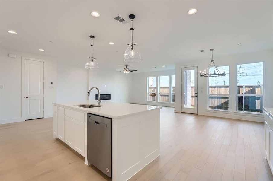 Kitchen featuring sink, hanging light fixtures, stainless steel dishwasher, a kitchen island with sink, and white cabinets