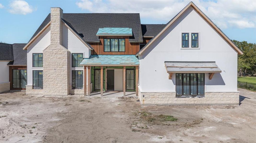 Rear view of property featuring a shingled roof, stone siding, and a chimney Rear view of property featuring a shingled roof, stone siding, and a chimney