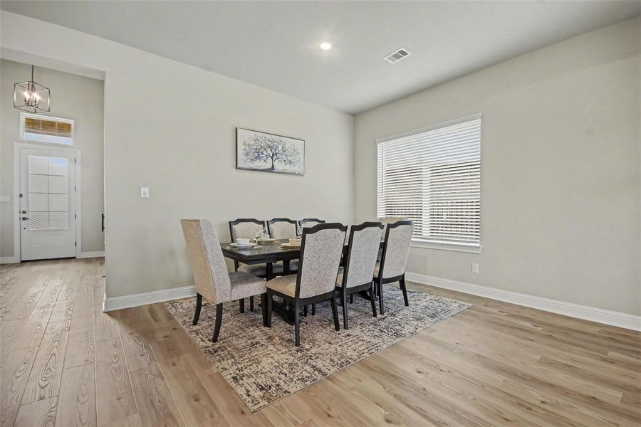 Bright dining area with a modern table set for six, elegant decor, and large window for natural light. Features light wood flooring and a welcoming entryway. Bright dining area with a modern table set for six, elegant decor, and large window for natural light. Features light wood flooring and a welcoming entryway.