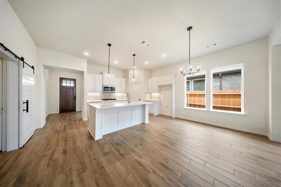 Kitchen with a barn door, light countertops, backsplash, a chandelier, and white cabinetry