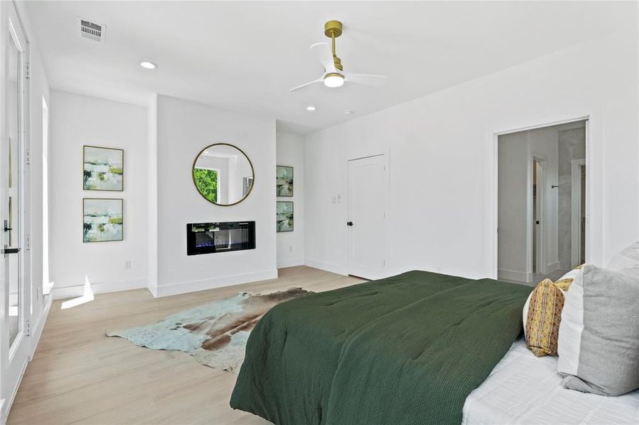 Bedroom featuring light wood finished floors, a glass covered fireplace, recessed lighting, and a ceiling fan Bedroom featuring light wood finished floors, a glass covered fireplace, recessed lighting, and a ceiling fan