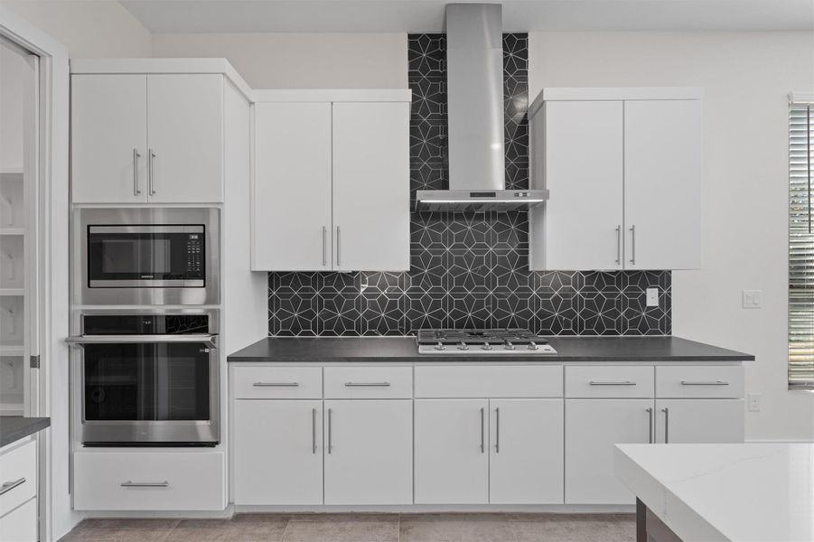 Kitchen with appliances with stainless steel finishes, wall chimney range hood, white cabinetry, and backsplash Kitchen with appliances with stainless steel finishes, wall chimney range hood, white cabinetry, and backsplash