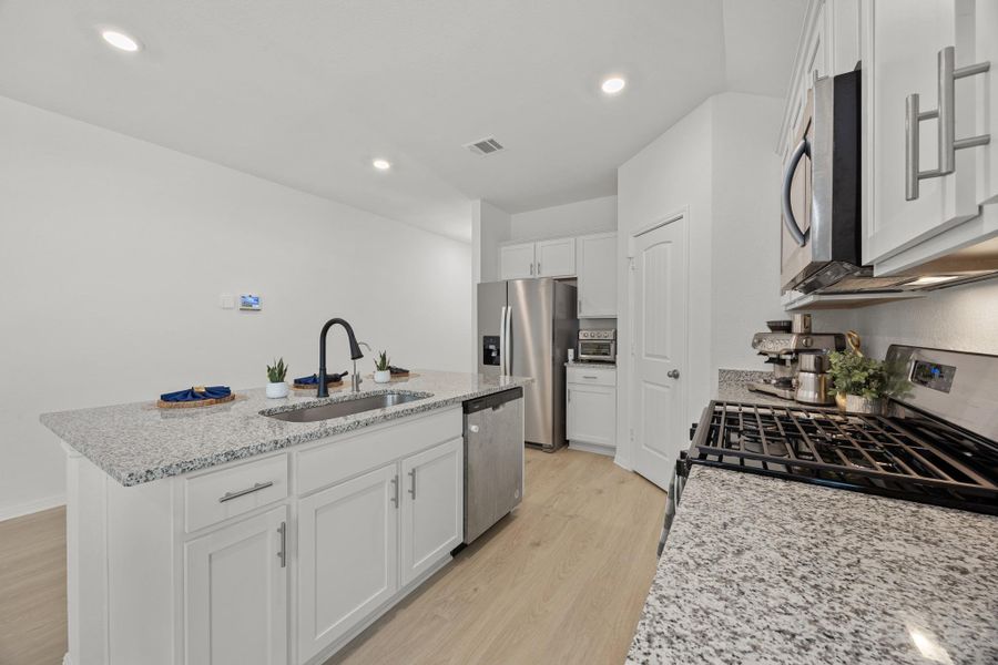 Kitchen featuring light stone countertops, an island with sink, stainless steel appliances, light wood-style flooring, and white cabinetry