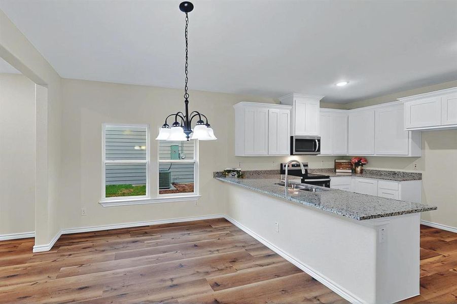 Kitchen with white cabinets, appliances with stainless steel finishes, an inviting chandelier, a sink, and a peninsula Kitchen with white cabinets, appliances with stainless steel finishes, an inviting chandelier, a sink, and a peninsula