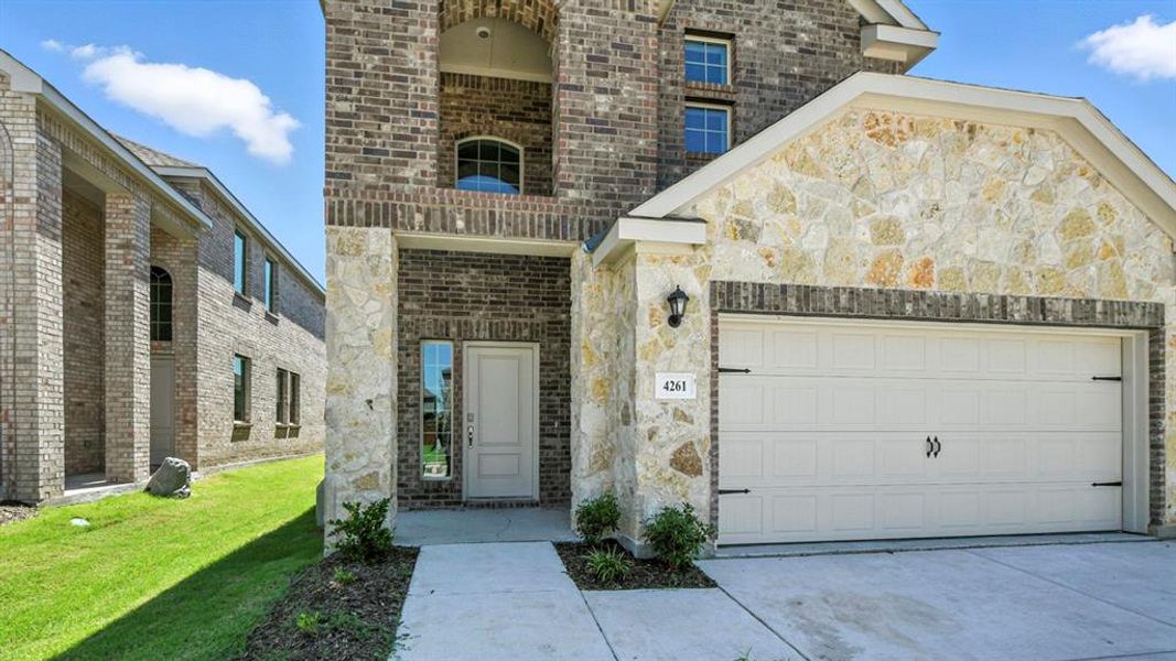 Doorway to property featuring brick siding, a yard, stone siding, concrete driveway, and a garage Doorway to property featuring brick siding, a yard, stone siding, concrete driveway, and a garage