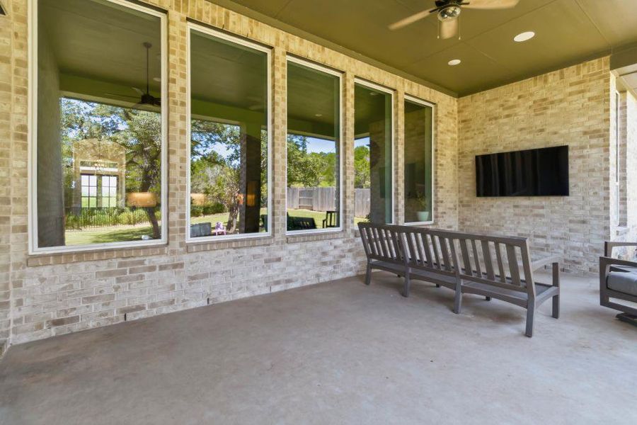 An inviting covered patio offers ample space for outdoor living, featuring a ceiling fan and generous windows overlooking a verdant yard.