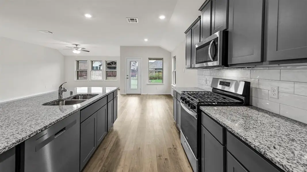 Kitchen featuring granite countertops, stainless steel appliances, dark wood cabinetry, and wood-finish flooring
