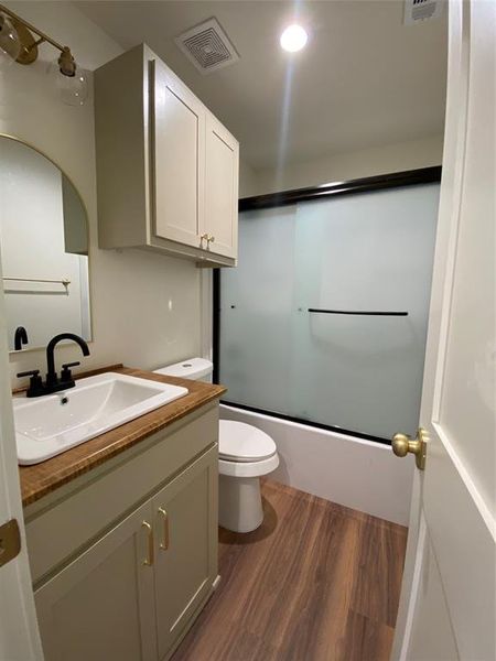 Hall bathroom featuring toilet, vanity, hardwood / wood-style floors, and bath / shower combo with glass door