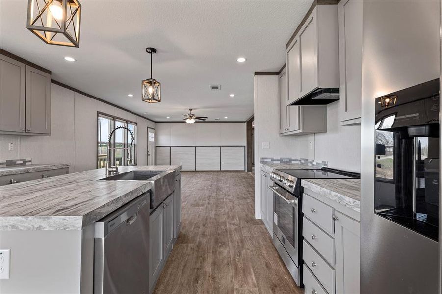 Kitchen with stainless steel appliances, gray cabinets, light countertops, open floor plan, and dark wood-style floors