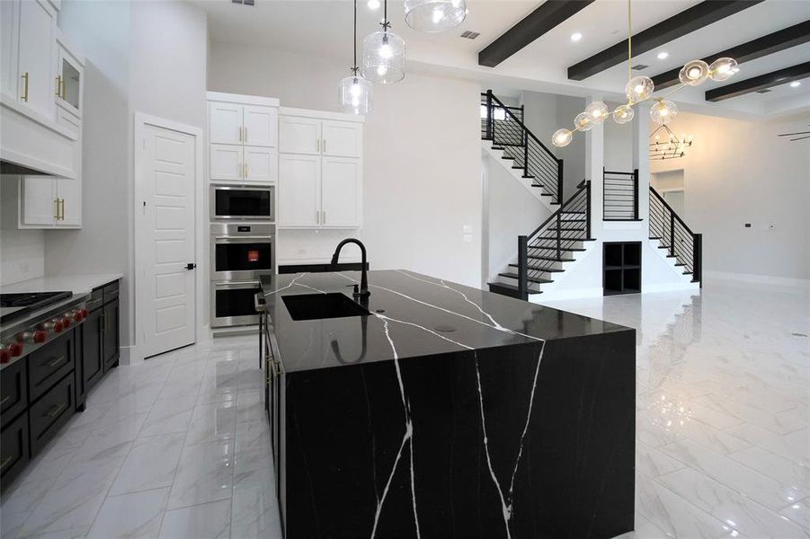 Kitchen featuring stainless steel appliances, a kitchen island with sink, sink, beamed ceiling, and white cabinets