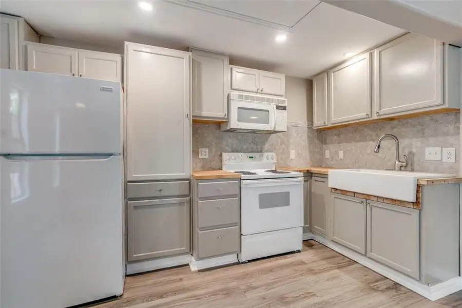Kitchen with white appliances, light wood-style floors, wooden counters, recessed lighting, and backsplash Kitchen with white appliances, light wood-style floors, wooden counters, recessed lighting, and backsplash