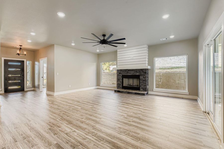 Unfurnished living room featuring light wood-style floors, ceiling fan, recessed lighting, and a stone fireplace