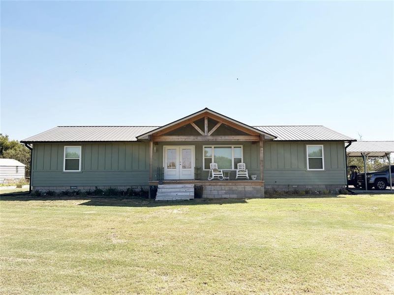 View of front of house featuring a metal roof, a front yard, covered porch, and board and batten siding View of front of house featuring a metal roof, a front yard, covered porch, and board and batten siding