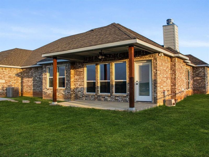 Rear view of property with brick siding, a yard, a chimney, a patio, and roof with shingles