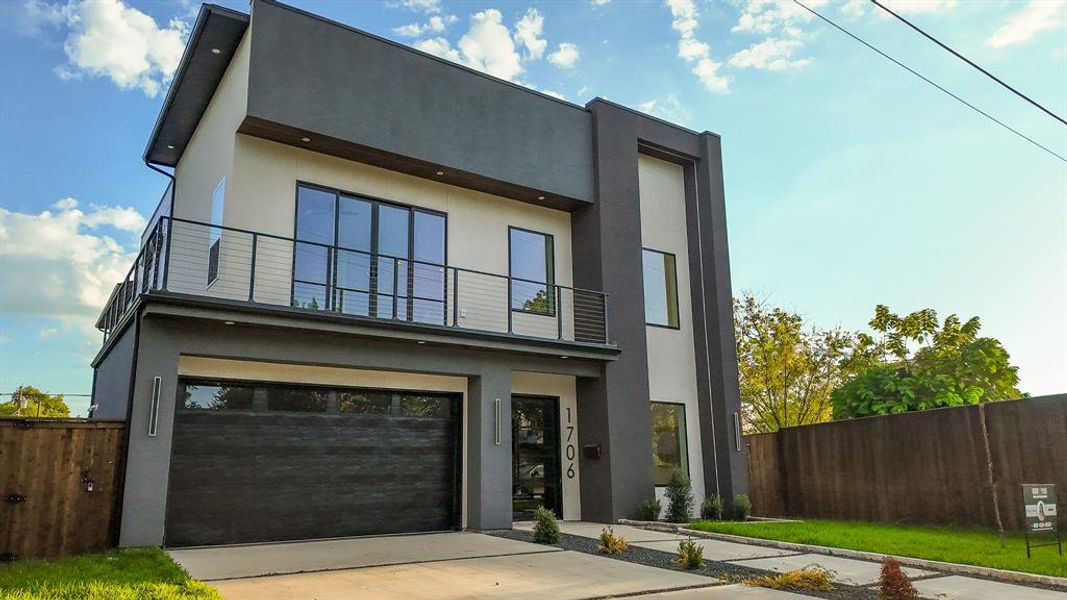 Modern home with an attached garage, stucco siding, a balcony, and driveway