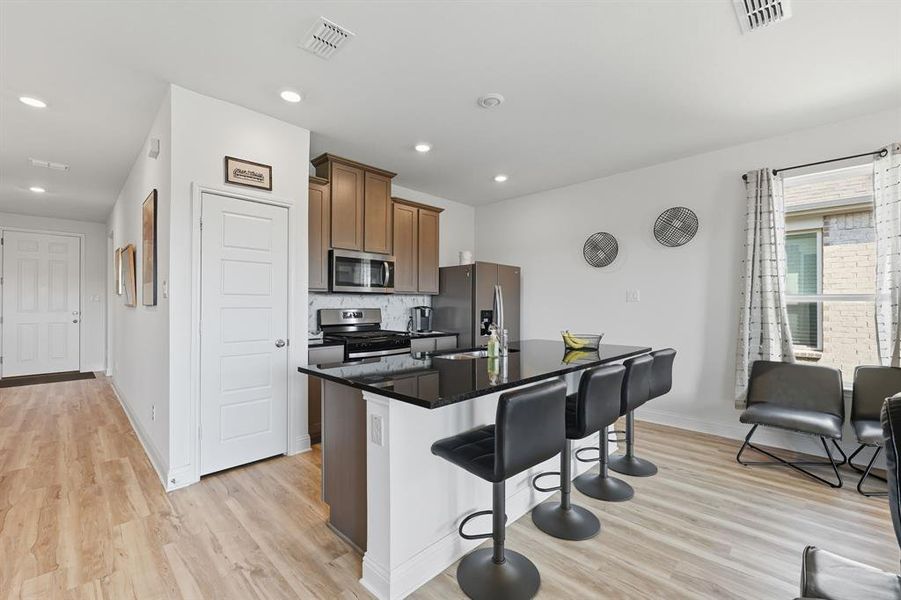 Kitchen featuring a center island with sink, light wood-style floors, stainless steel appliances, a breakfast bar, and recessed lighting Kitchen featuring a center island with sink, light wood-style floors, stainless steel appliances, a breakfast bar, and recessed lighting