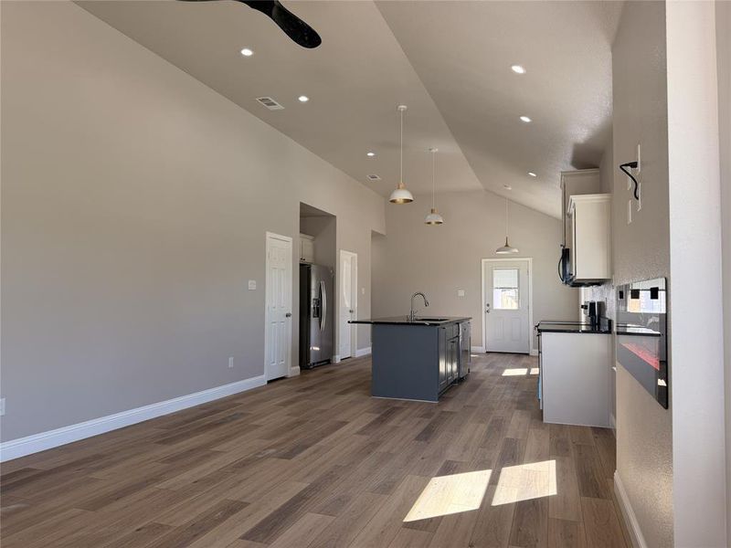 Kitchen with an island with sink, dark wood-style flooring, a ceiling fan, stainless steel refrigerator with ice dispenser, and open floor plan
