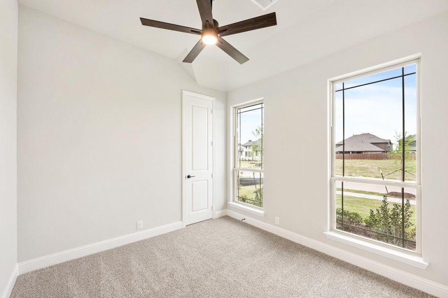 Empty bedroom with carpet, ceiling fan, and two windows overlooking a yard Empty bedroom with carpet, ceiling fan, and two windows overlooking a yard