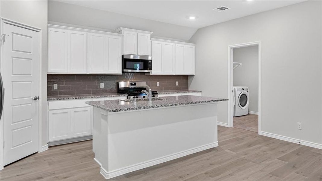 Modern kitchen featuring white shaker cabinetry, stainless steel appliances, a grey subway tile backsplash, and light wood-finish flooring