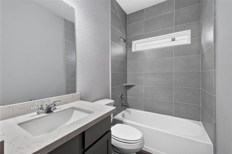 This bathroom features a modern design with sleek gray tiles, a white bathtub, and a compact vanity. A small window provides natural light, enhancing the clean, contemporary feel. This bathroom features a modern design with sleek gray tiles, a white bathtub, and a compact vanity. A small window provides natural light, enhancing the clean, contemporary feel.