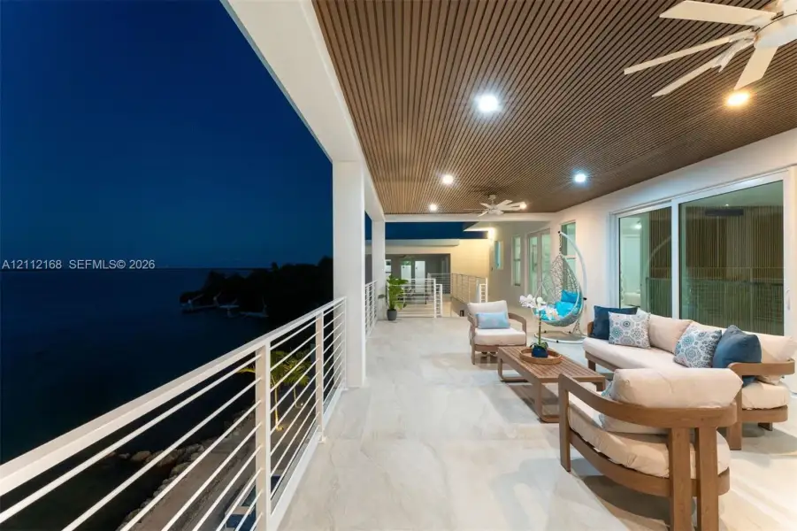Covered balcony featuring a slatted wood-finish ceiling, large-format tile flooring, recessed lighting, ceiling fans, and a horizontal cable railing system Covered balcony featuring a slatted wood-finish ceiling, large-format tile flooring, recessed lighting, ceiling fans, and a horizontal cable railing system