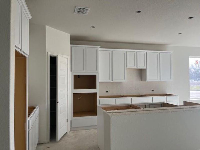 Kitchen featuring black electric stovetop, concrete floors, a kitchen island, visible vents, and white cabinetry