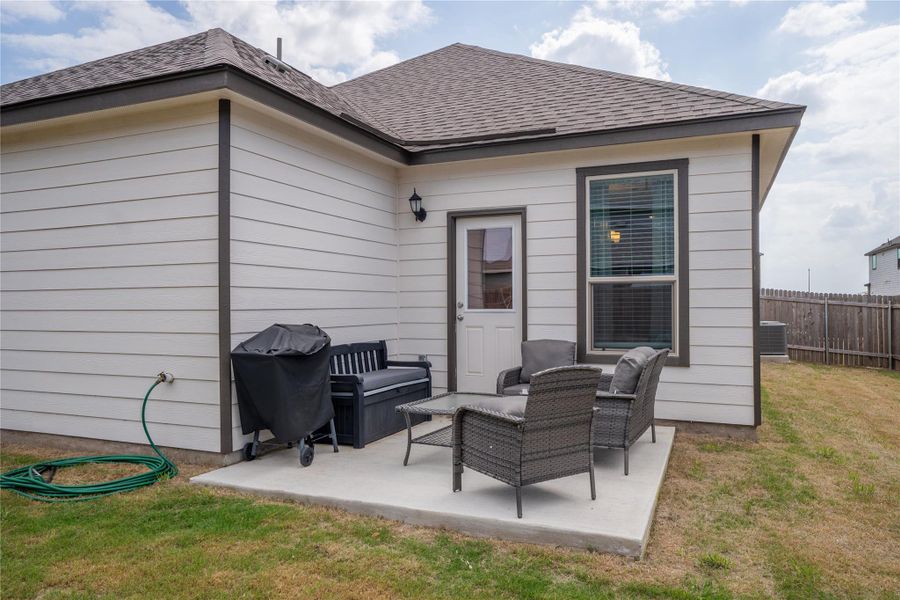 Rear exterior featuring a concrete patio, white horizontal siding, a framed window with blinds, and a rear entry door Rear exterior featuring a concrete patio, white horizontal siding, a framed window with blinds, and a rear entry door