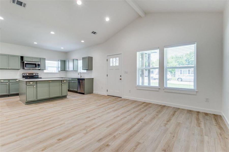 Kitchen with stainless steel appliances, light wood-type flooring, a center island, beam ceiling, and green cabinetry